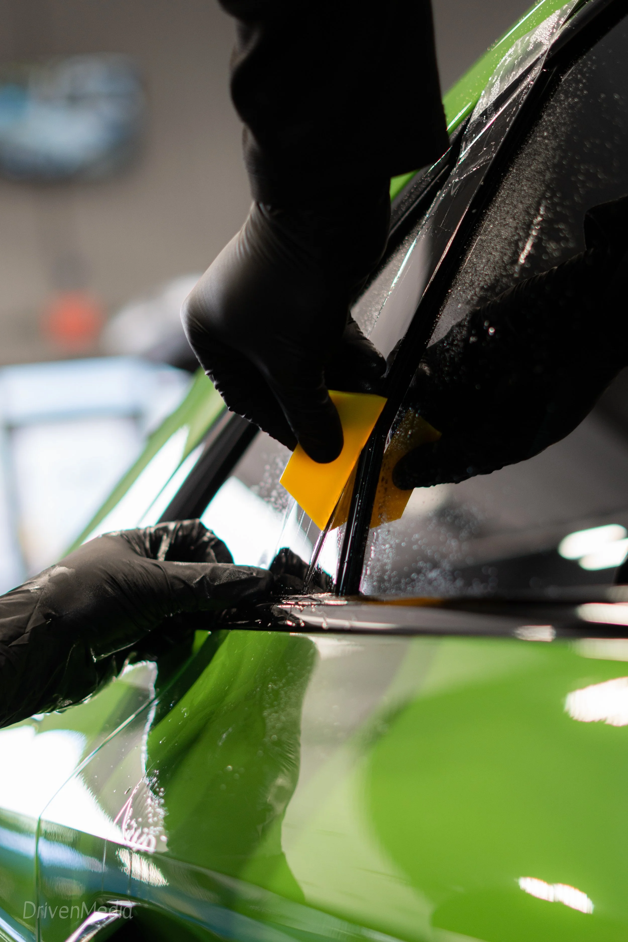 A person wearing black gloves using a yellow squeegee to clean a car window.
