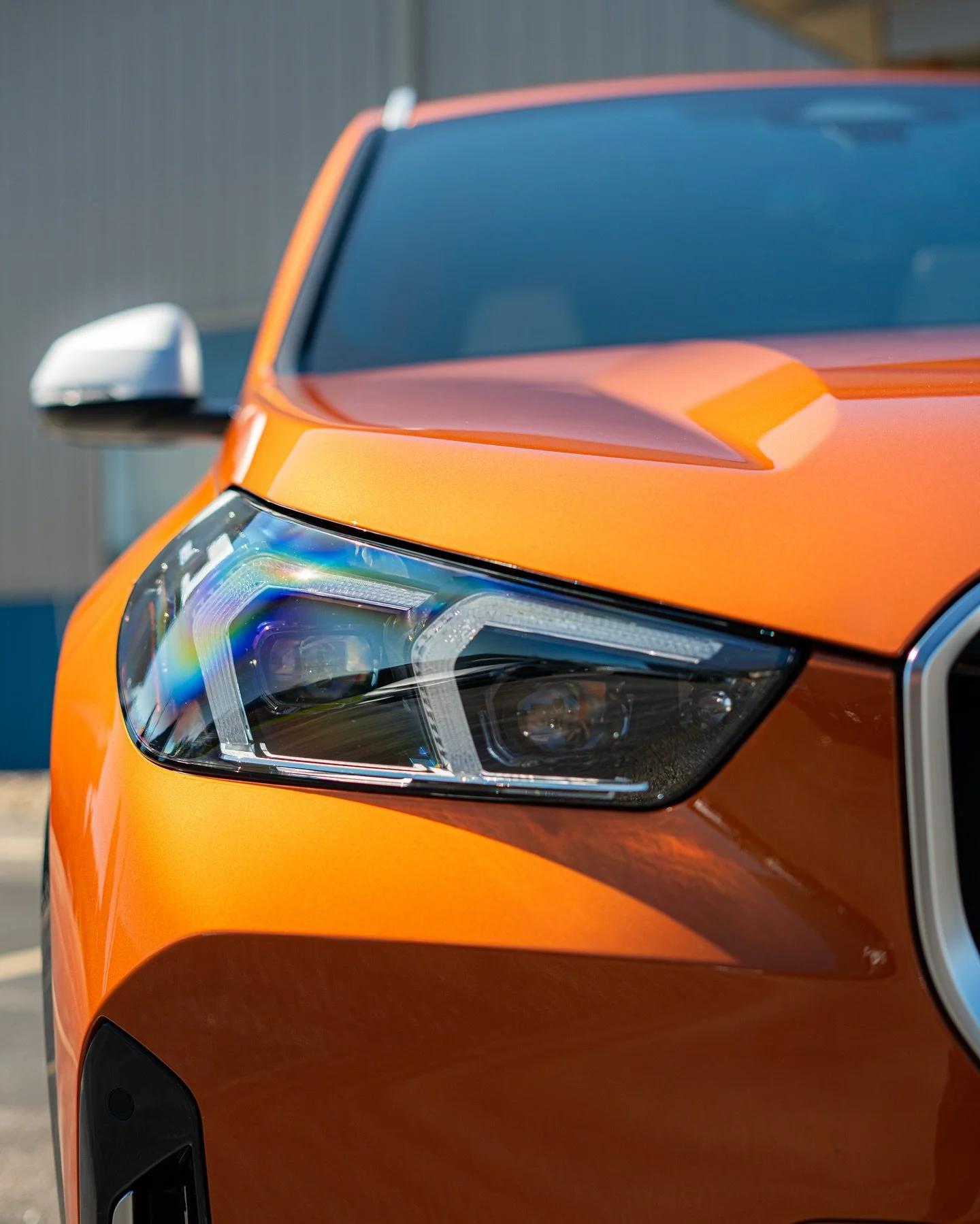 Close-up of the front part of an orange car, showing the headlight and part of the windshield.
