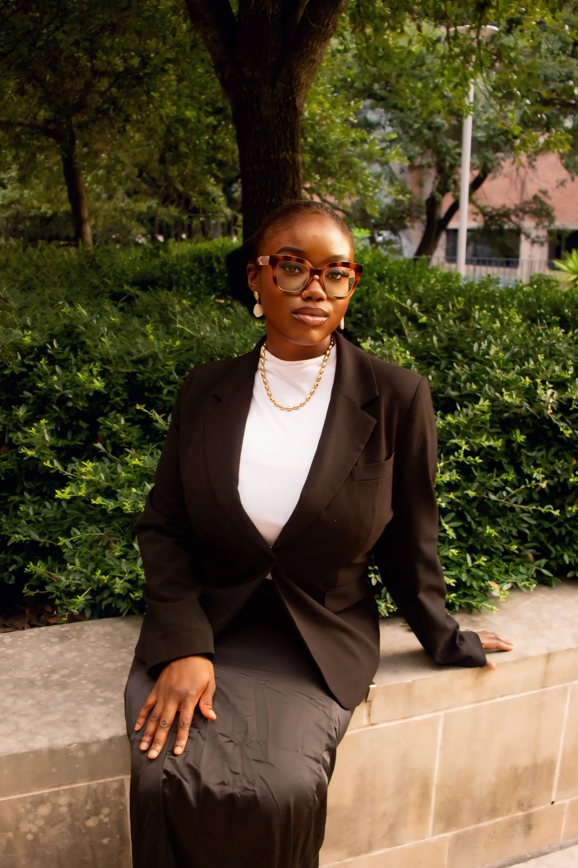 Person with glasses and braided hair wearing a light pink blazer, smiling in a professional setting.