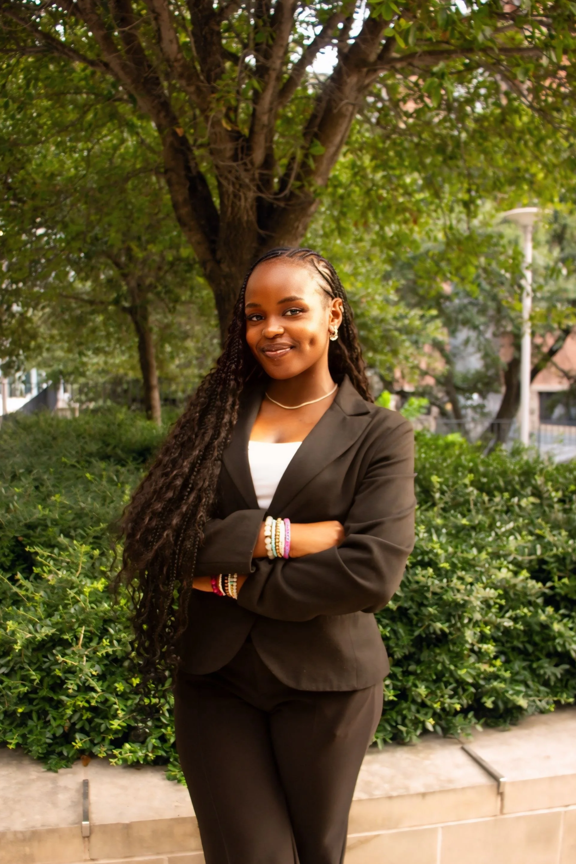 Woman with braids wearing a white shirt and brown top against a neutral indoor background.