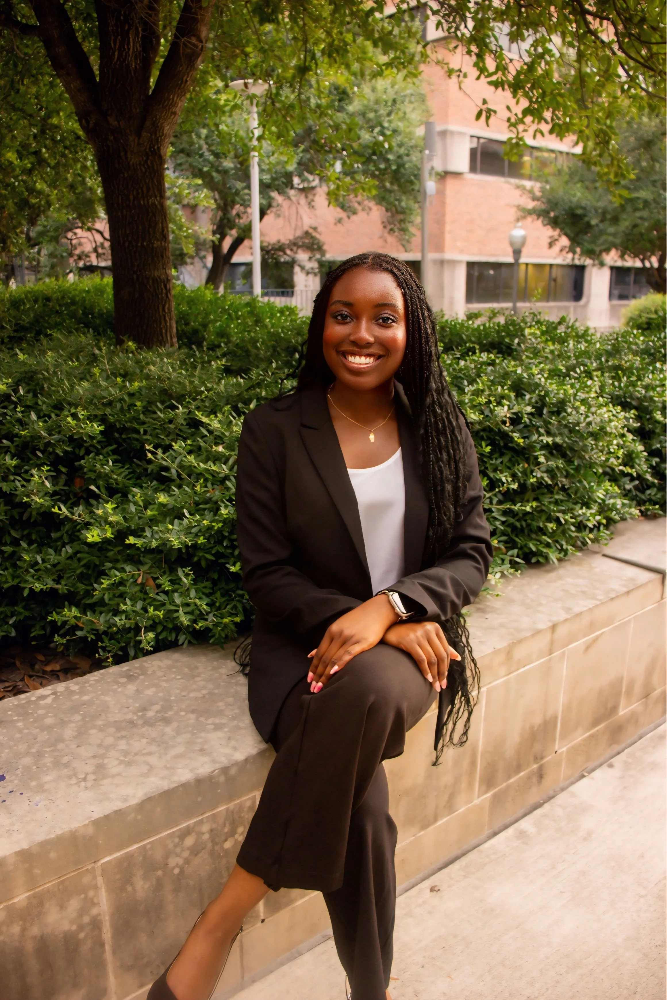 Confident woman with short curly hair wearing a sleeveless pink top, standing indoors with crossed arms.