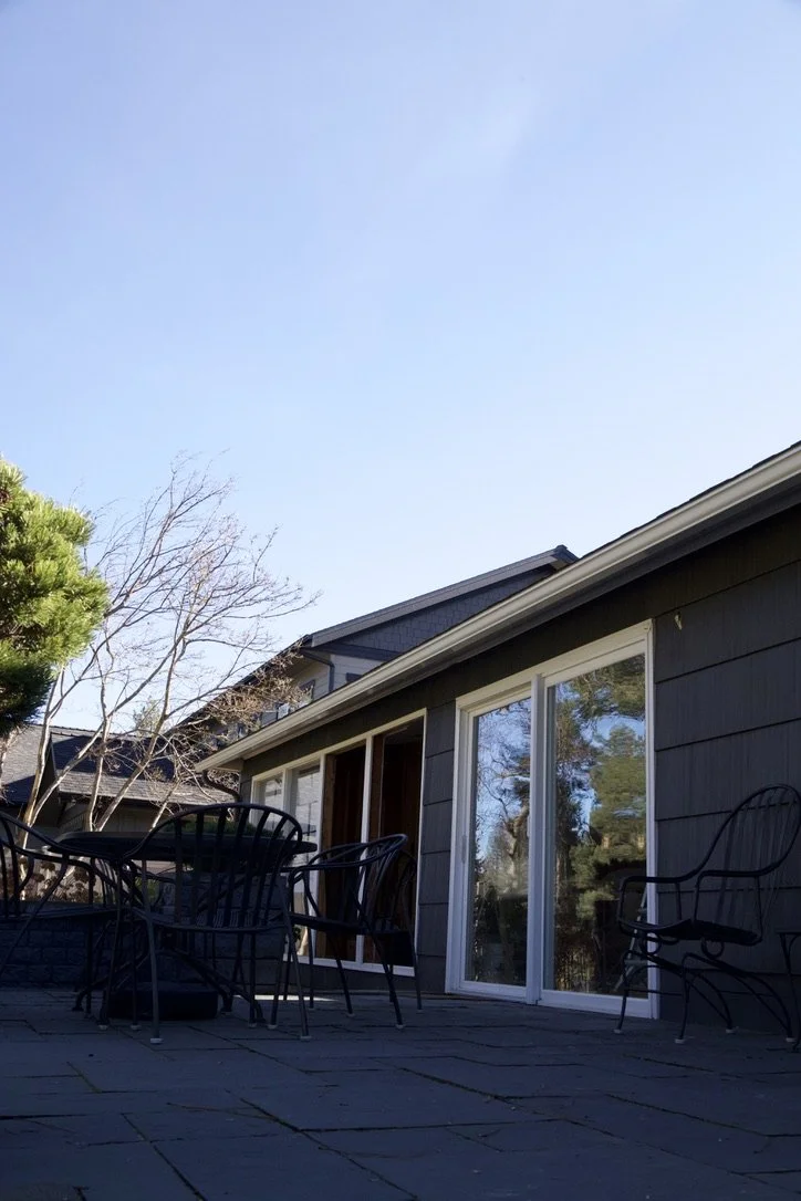 An outdoor patio with black metal chairs and a sliding glass door leading into a house, under a clear blue sky.