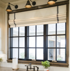Kitchen window with black framing, white Roman shade, and a wooden light fixture above, with a small potted plant and soap dispensers on the countertop.