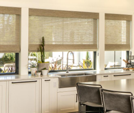 Kitchen with white cabinets, large windows with blinds, and a countertop with a sink and plants.