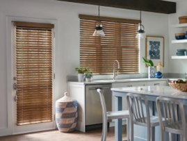 Kitchen with white cabinets, wooden blinds on windows, a white island with chairs, and shelves with dishes and decor.