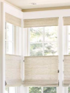 Close-up of white window blinds partially raised, revealing sunlight and a view of trees outside.