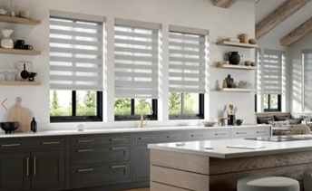 Modern kitchen with white and gray cabinetry, large windows with striped blinds, a white countertop, and open shelves with decorative items.