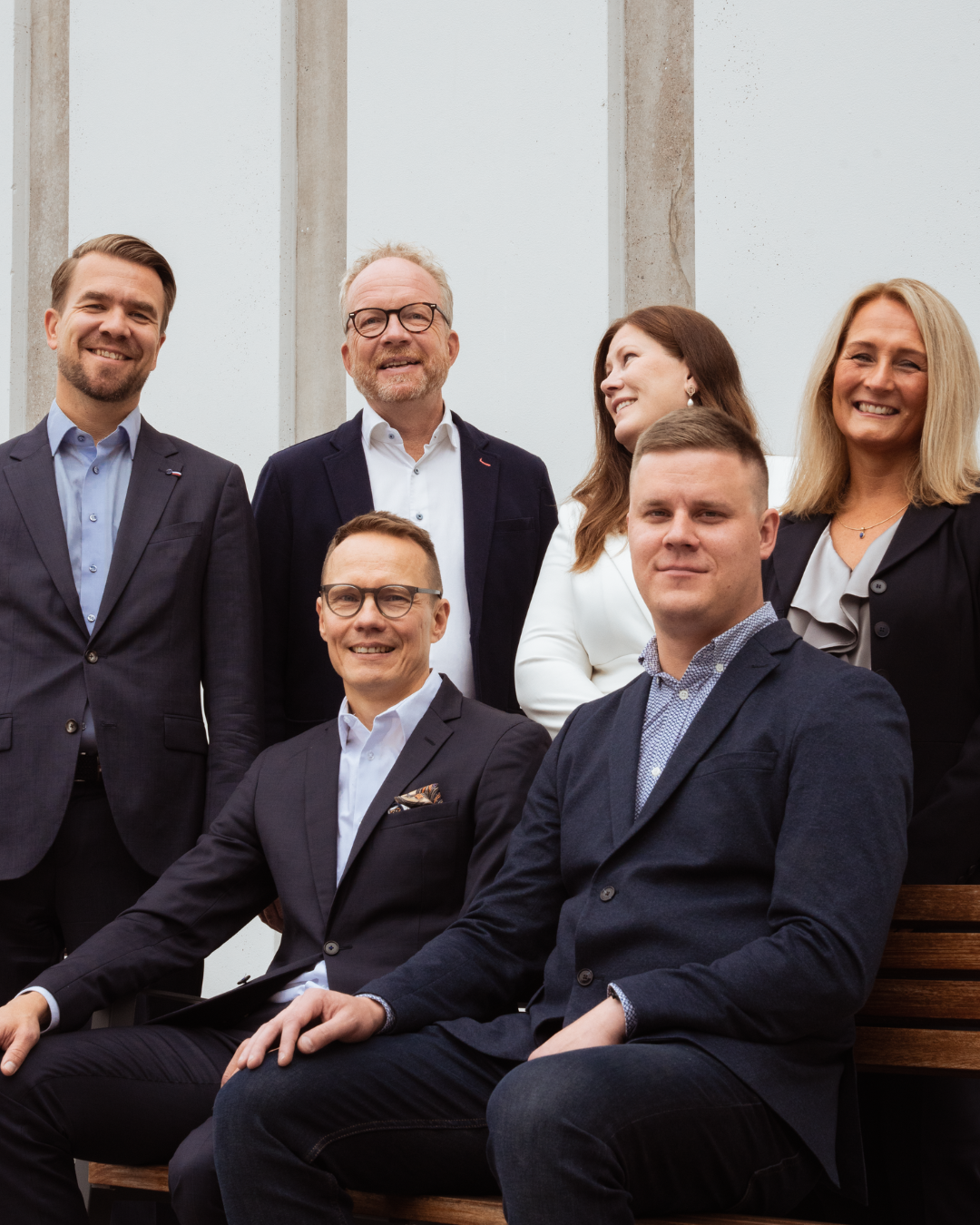 Group of six professional people posing for a photo in an office setting, smiling and dressed in business attire.