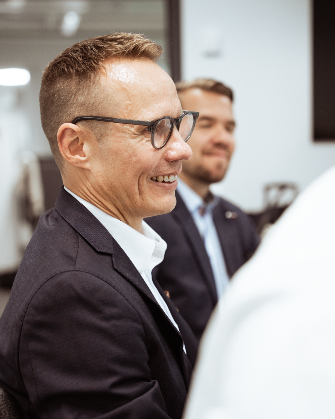 Two men in business suits smiling during a meeting in an office.