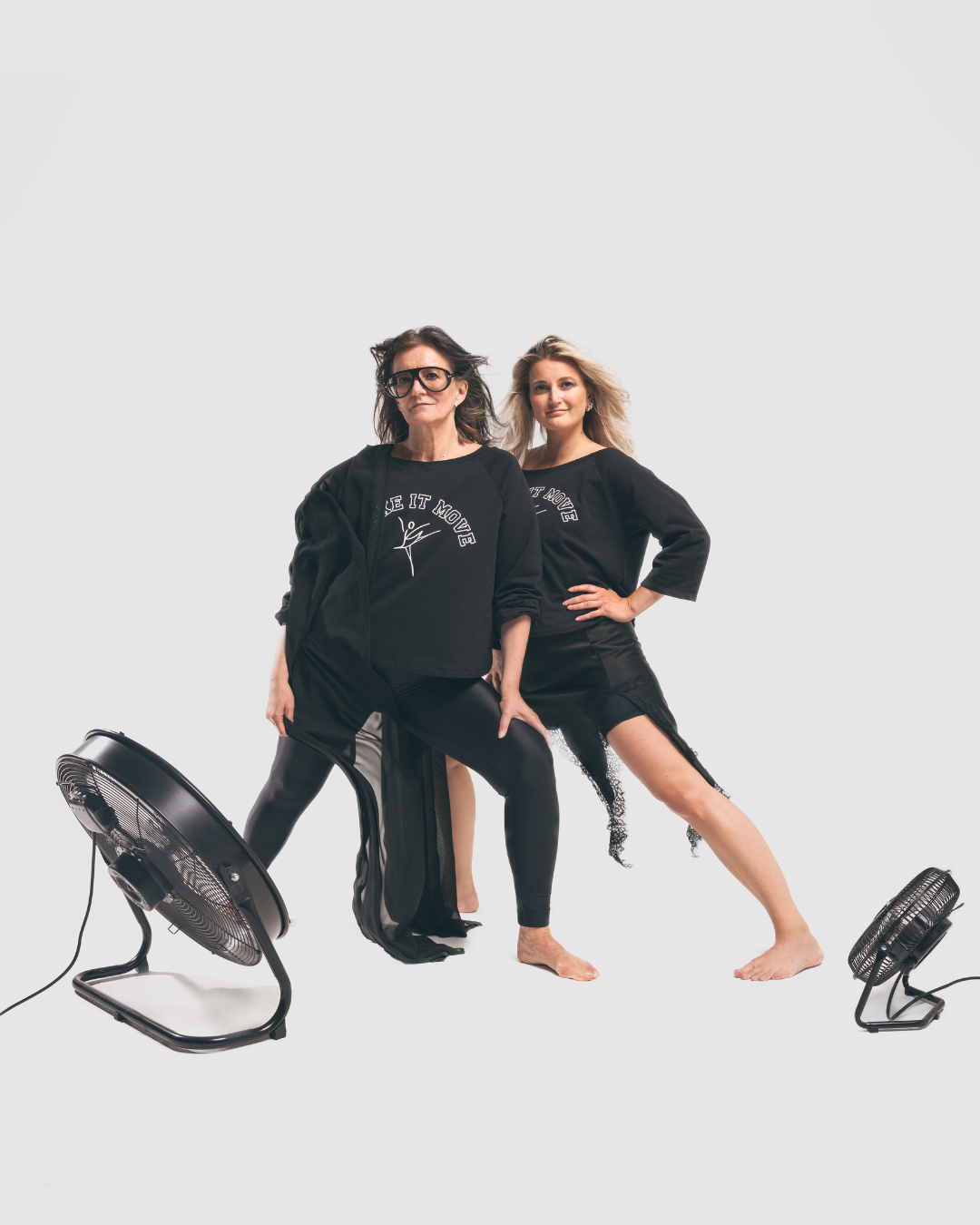 Two women in black workout clothes posing with fans on a white background.