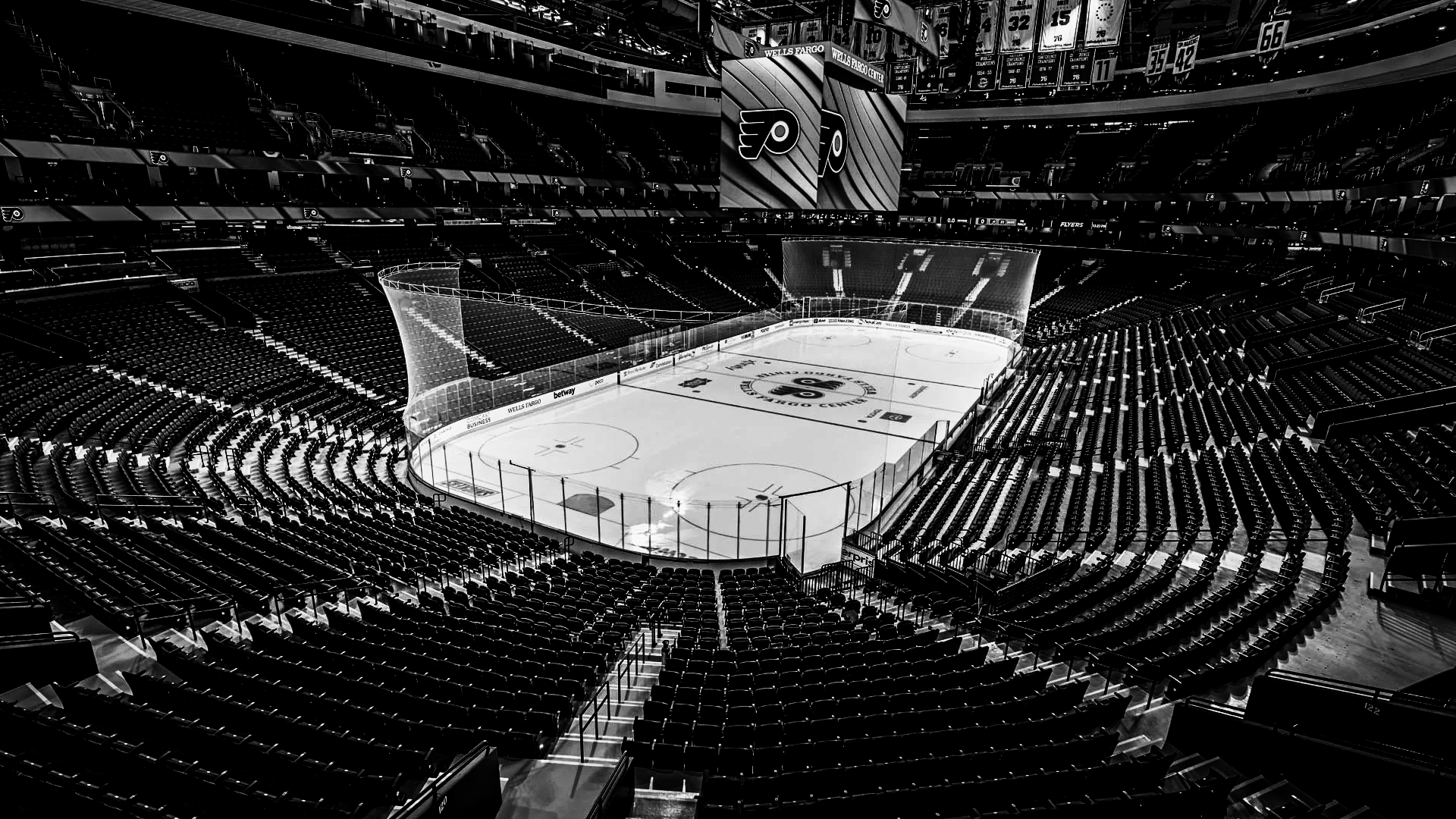 Empty ice hockey arena with seats surrounding the rink, scoreboard displaying the Philadelphia Flyers logo, and banners hanging from the ceiling.