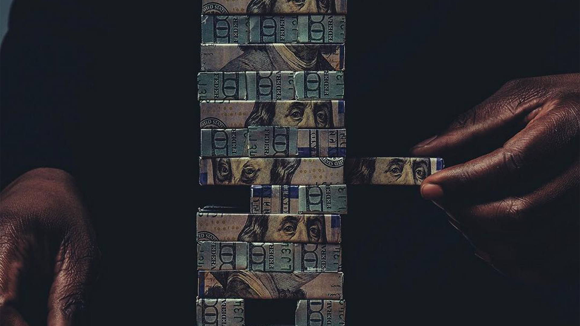 Hands assembling a Jenga tower made of 100-dollar bills against a black background.