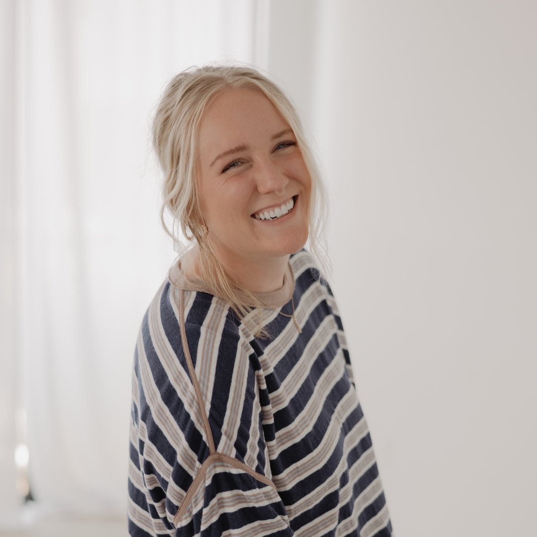 A young woman with blonde hair and a septum piercing smiling in a striped shirt.