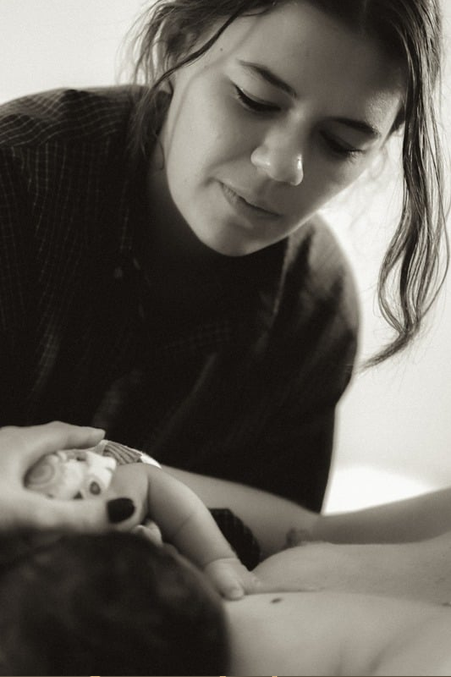 A labor doula gently helping a mom hold her baby while smiling softly.