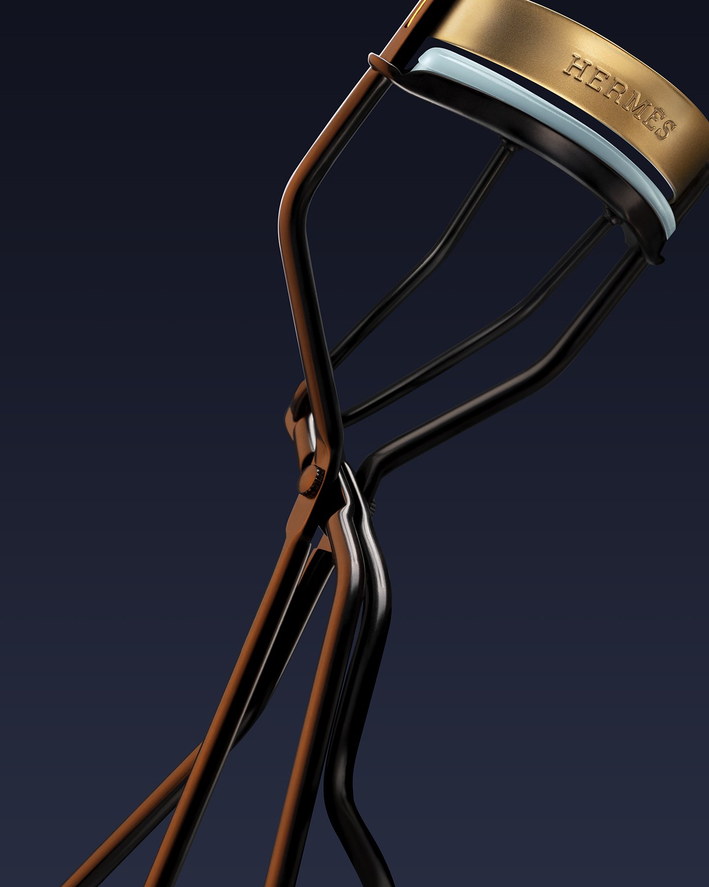 A close-up image of an eyelash curler with the Hermès logo on the gold cap, against a dark background.