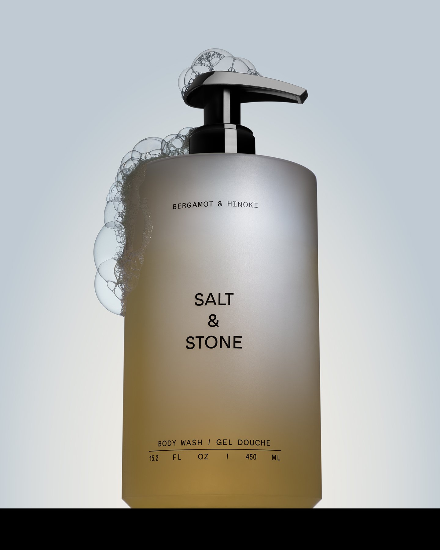 A bottle of body wash labeled 'Salt & Stone' with black pump and soap bubbles.