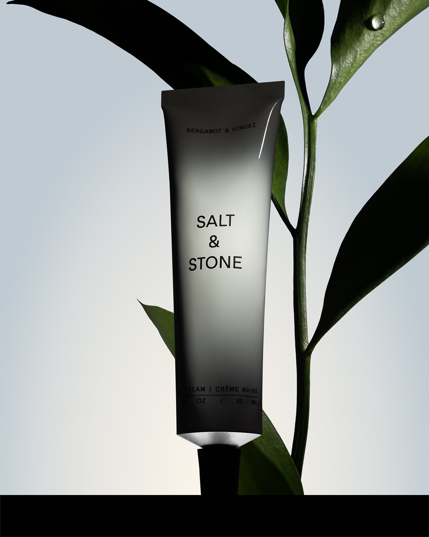 A black and white tube of Salt & Stone hand cream with green leafy plant in the background.