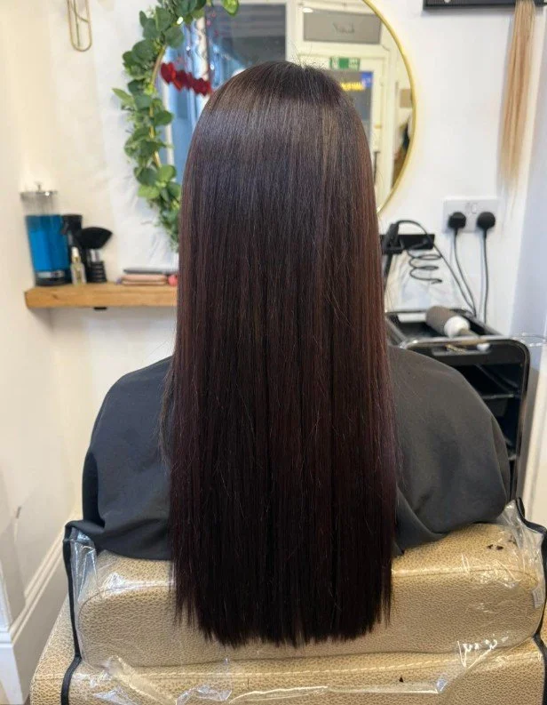 Back view of a woman with long, straight brown hair sitting in a salon chair.