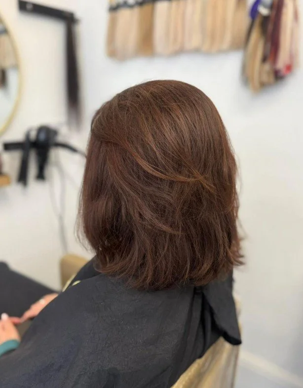 Back of a person's head with medium-length, brownish-red hair in a salon chair.
