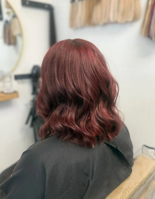 Woman with shoulder-length wavy red hair sitting in a salon chair.