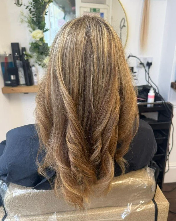 Back view of a woman with freshly styled, bouncy, layered light brown hair in a salon setting.