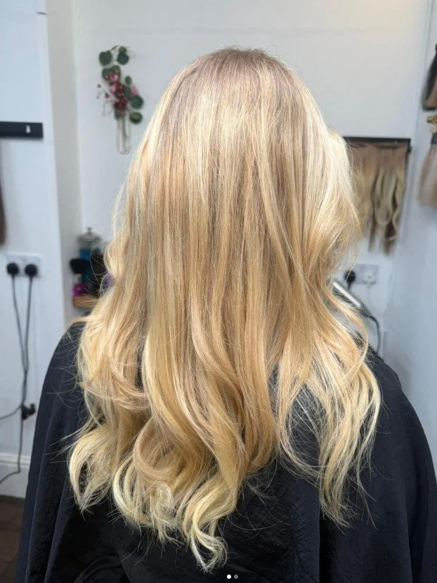 Back of a woman with long, wavy blonde hair in a hair salon.