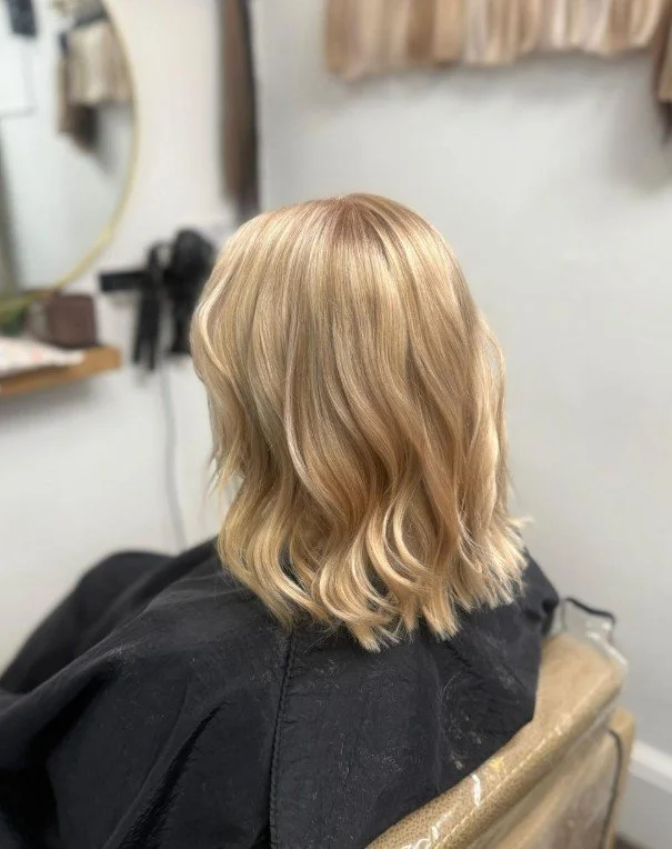 Blonde wavy shoulder-length hair seen from behind in a salon chair.