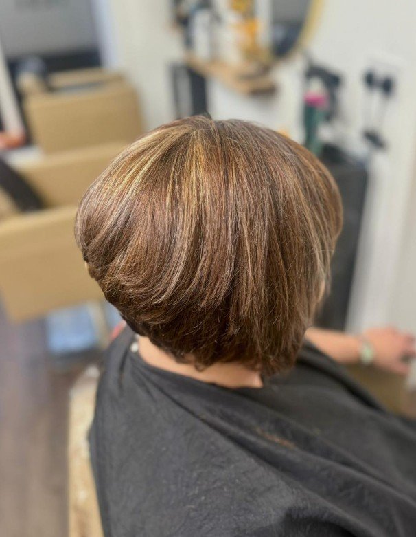 Back view of a woman with a short, layered haircut dyed in shades of light brown and blonde, sitting in a salon chair.
