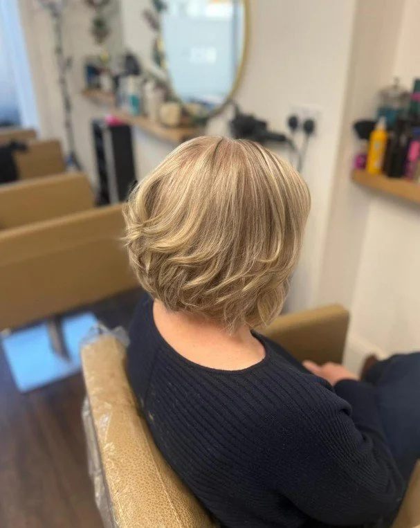 Woman with short, wavy blonde hair sitting in a salon chair.