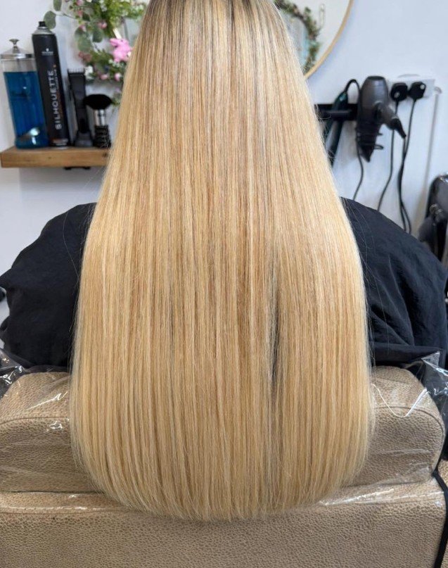 Back view of a woman with long, straight, blonde hair in a salon.