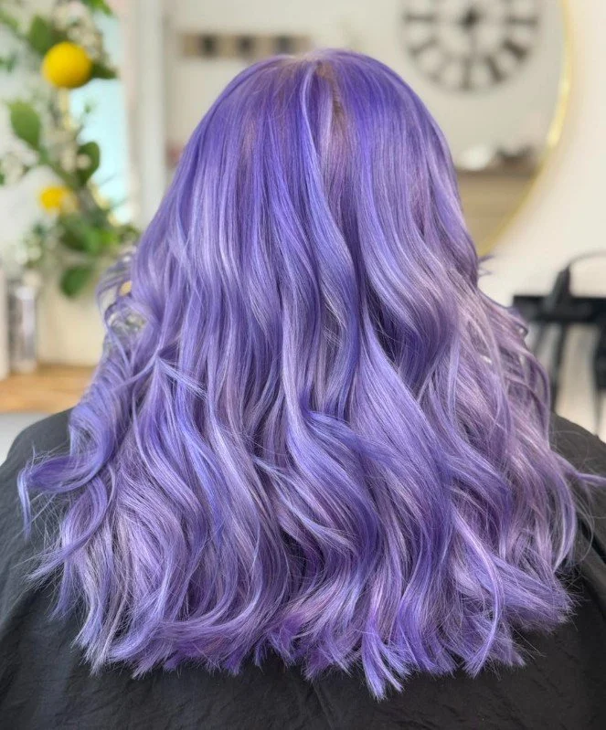 Back view of a woman with shoulder-length, wavy lavender to purple hair.