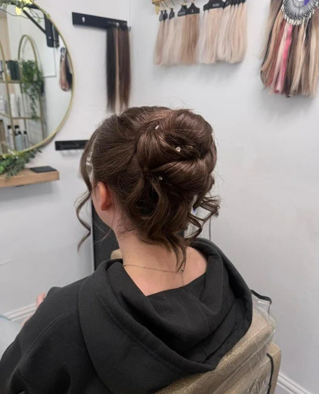 Back of a woman with curled hair in an updo, sitting in a salon chair.
