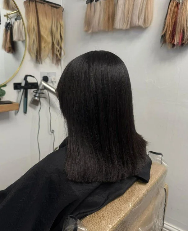 Back view of a woman with straight, shiny black hair, sitting in a salon chair.