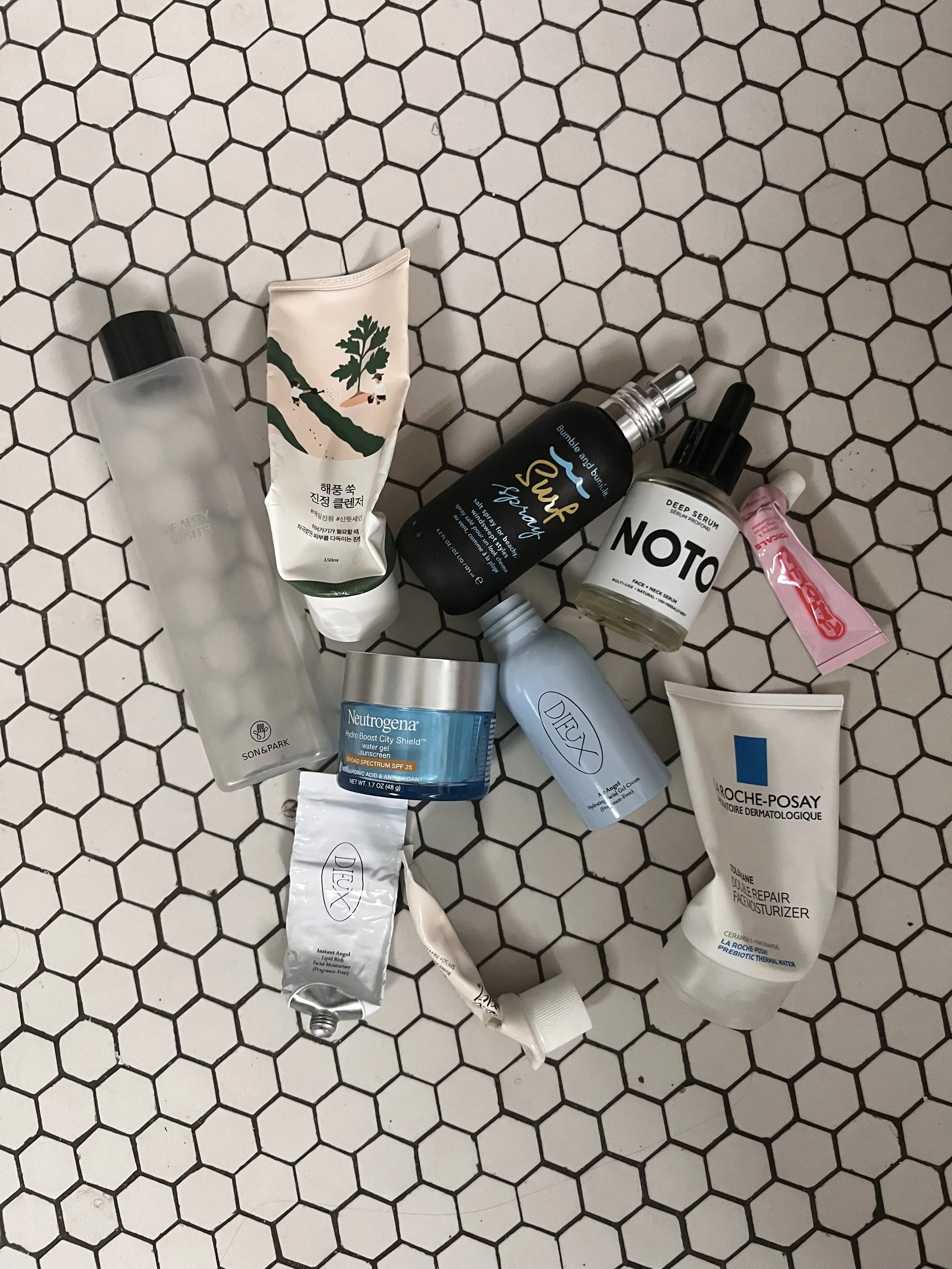 A layout of various skincare products on a hexagonal black and white tiled surface, including tubes and jars from brands like Neutrogena and La Roche-Posay.