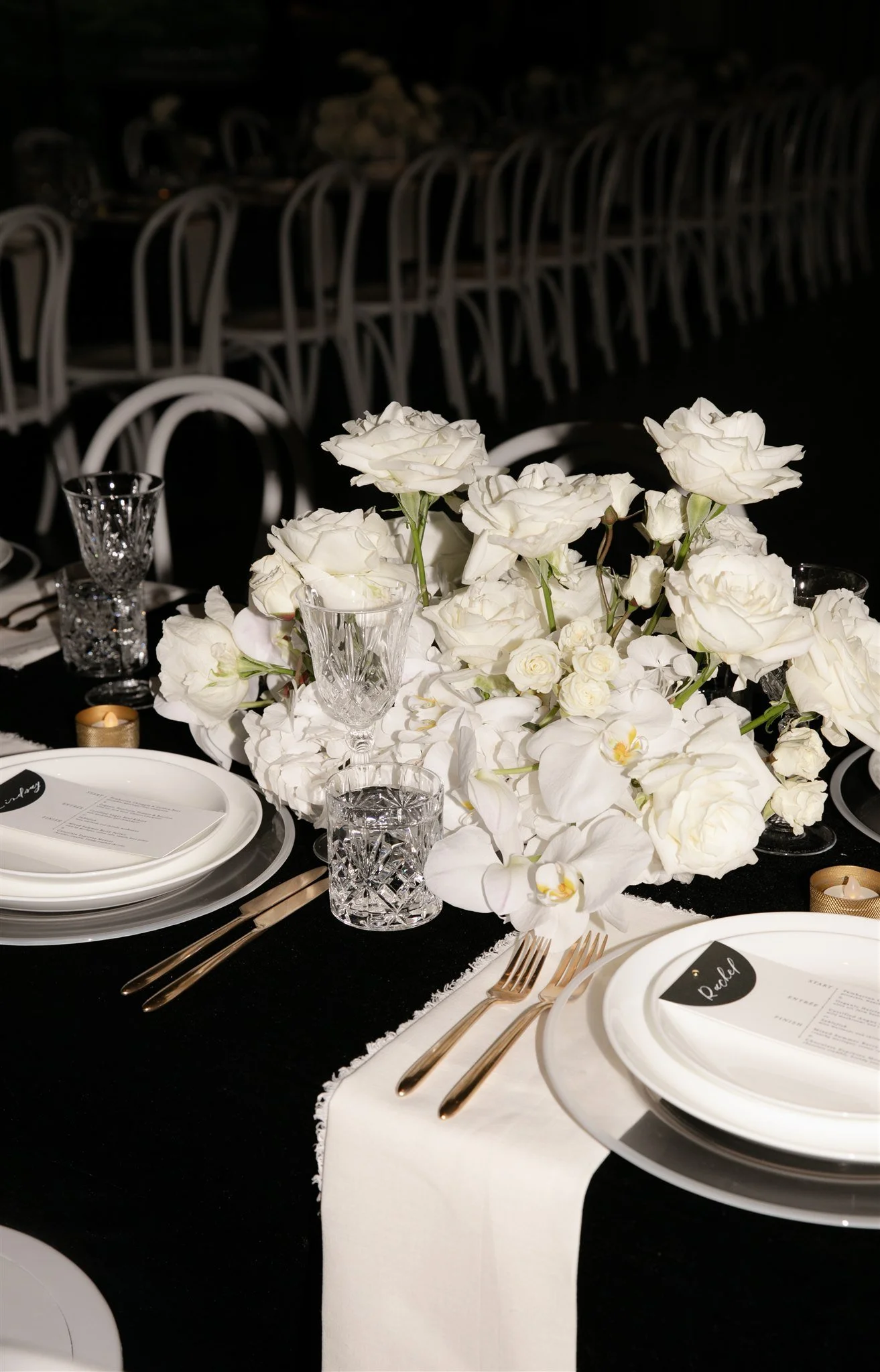 Elegant table setting with white flowers centerpiece, glassware, gold cutlery, and black and white tableware at wedding Audain Art Museum.