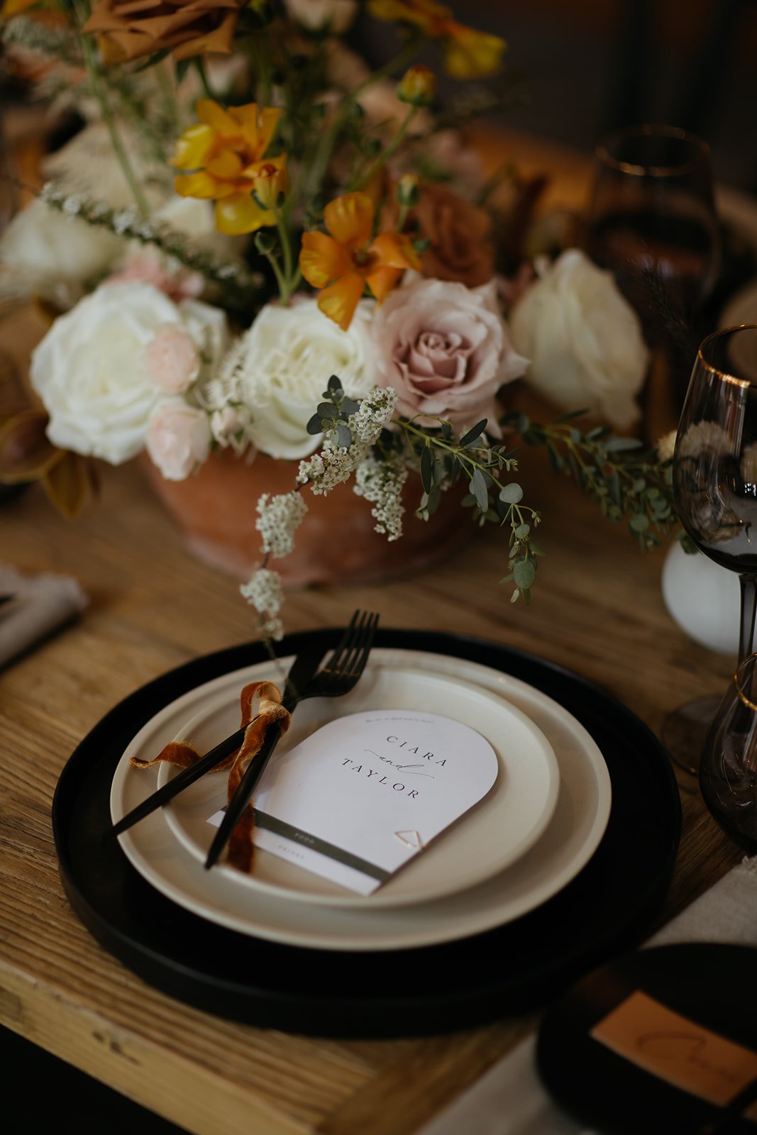 Wedding reception table with a floral centerpiece, place settings, and a menu card reading 'Clara and Taylor'.