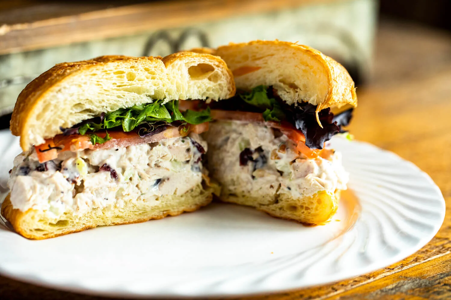 Chicken salad sandwich on a croissant with lettuce and tomato, served on a white plate.