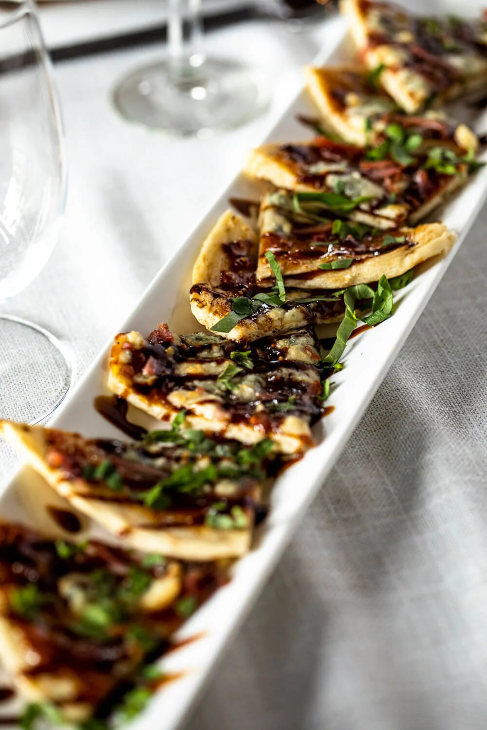 Slices of flatbread topped with cheese, greens, and a drizzle of balsamic glaze on a rectangular white plate.