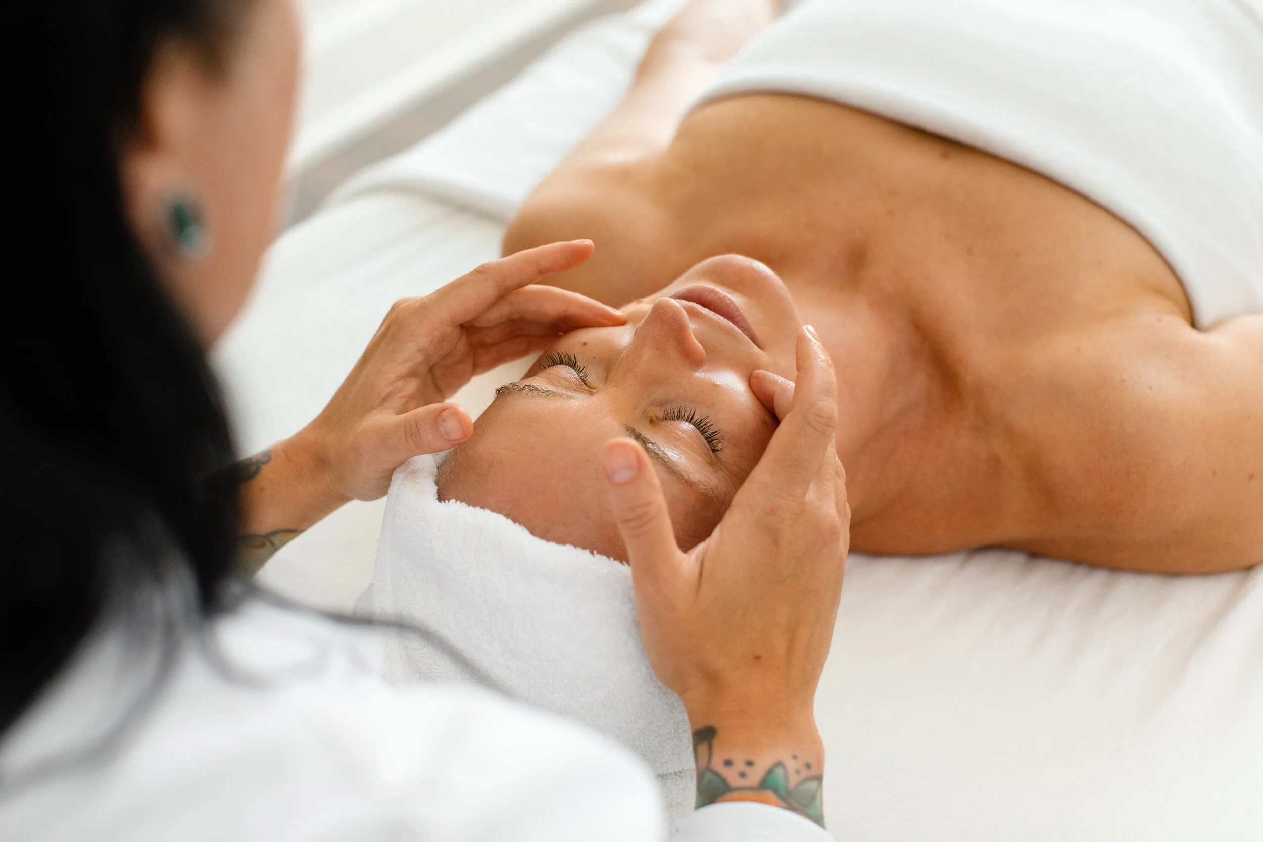 A woman receiving a facial massage from an esthetician in a spa setting.