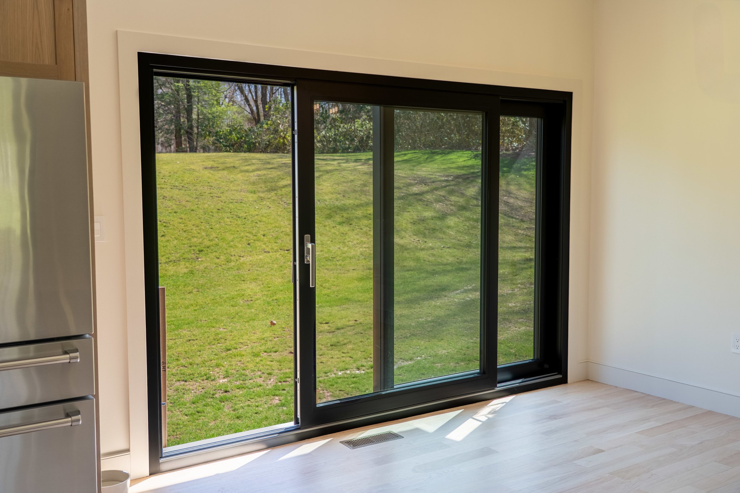 Sliding glass door with black frame leading to a grassy lawn, interior view with part of a refrigerator visible on the left.