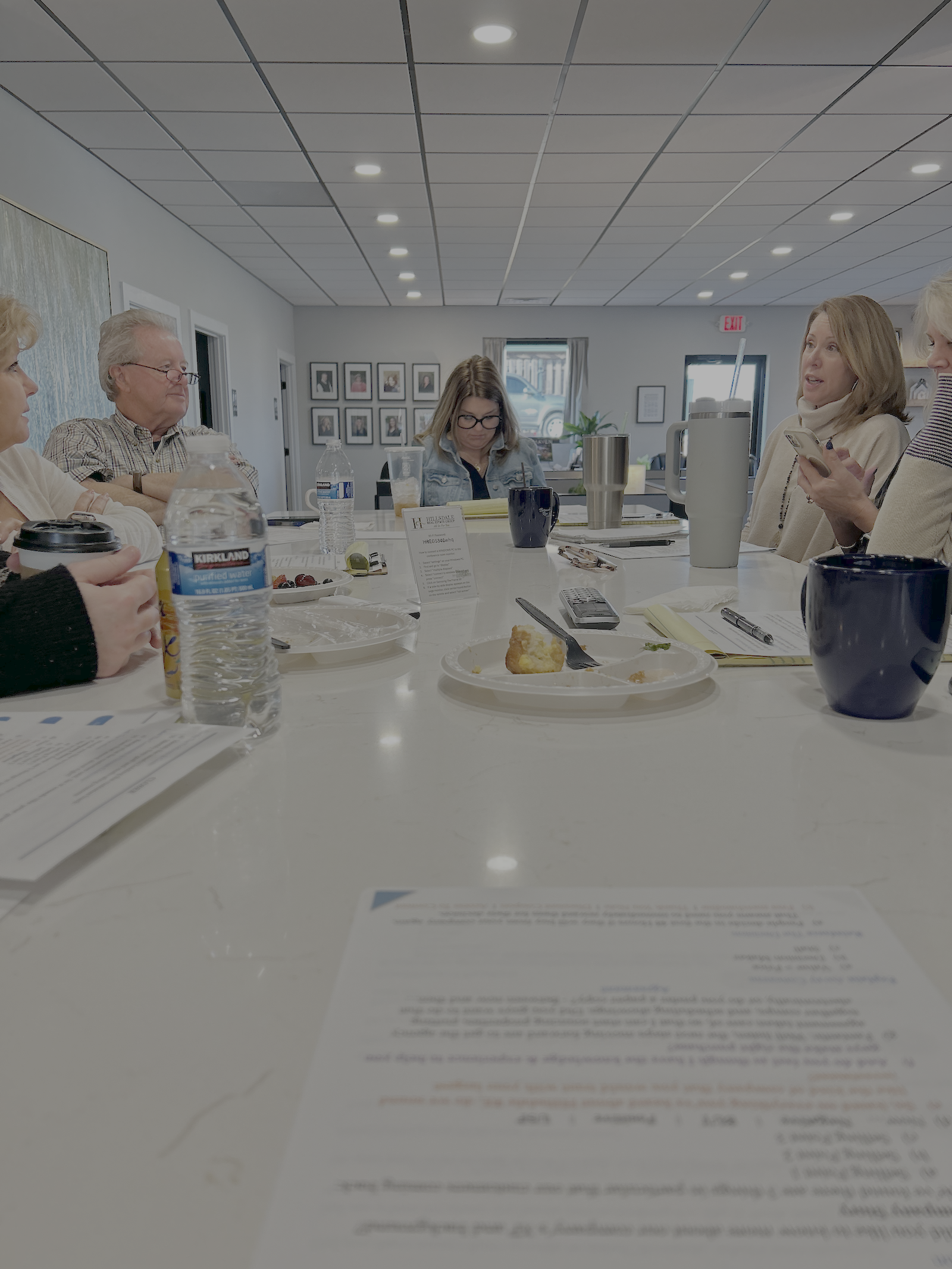 A group of six people sitting around a white conference table having a sales management meeting.