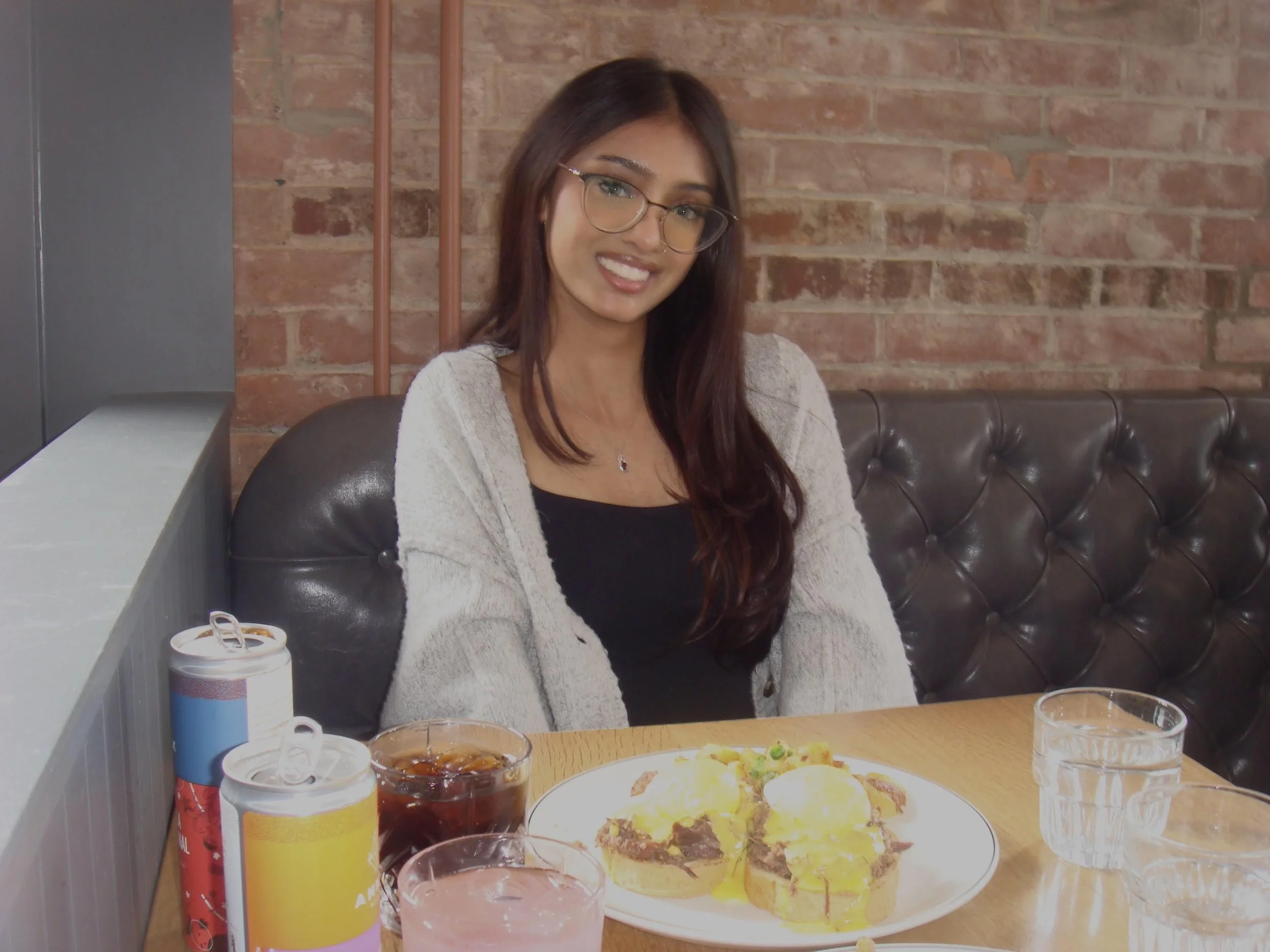 Smiling woman with short black hair wearing a blue blouse, standing outdoors in a garden setting.