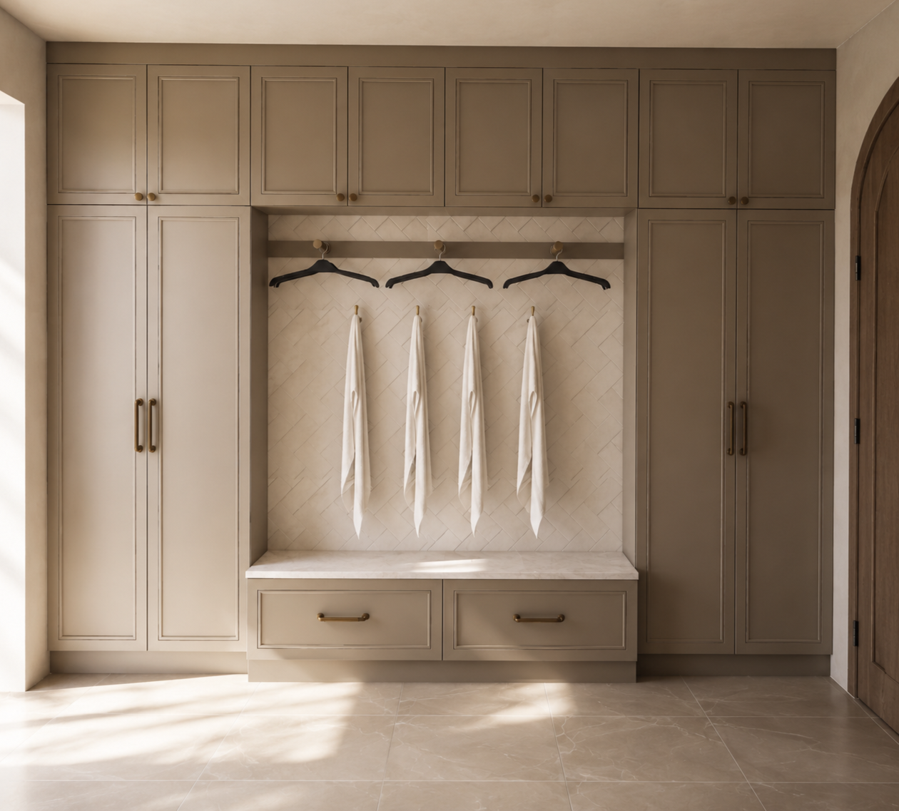 Built-in beige wardrobe with cabinets and drawers, a small open area with hanging clothes and empty hangers, and a tiled wall backdrop in a modern laundry room or closet.