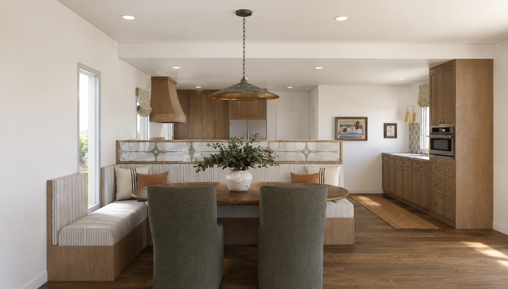 Dining area with built-in corner seating, a round wooden table with a white vase and green foliage, and two green chairs. The space has wooden floors, white walls, and natural light from windows. The kitchen is visible in the background with wooden c
