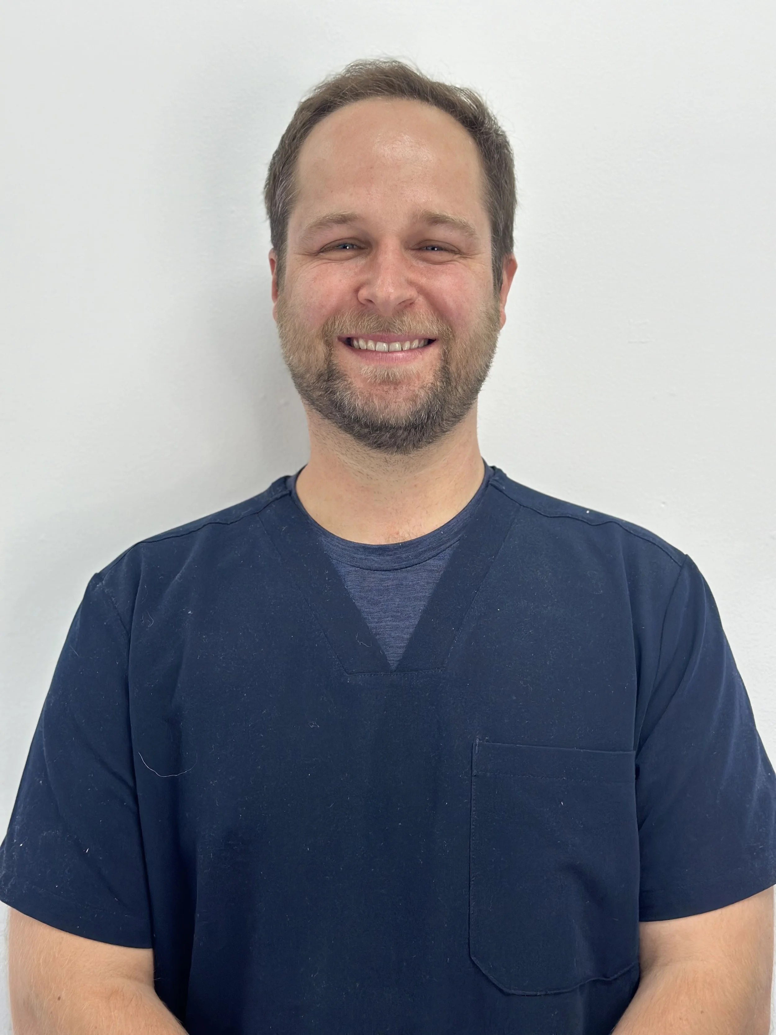 Person in dark blue scrub top smiling against a white background.