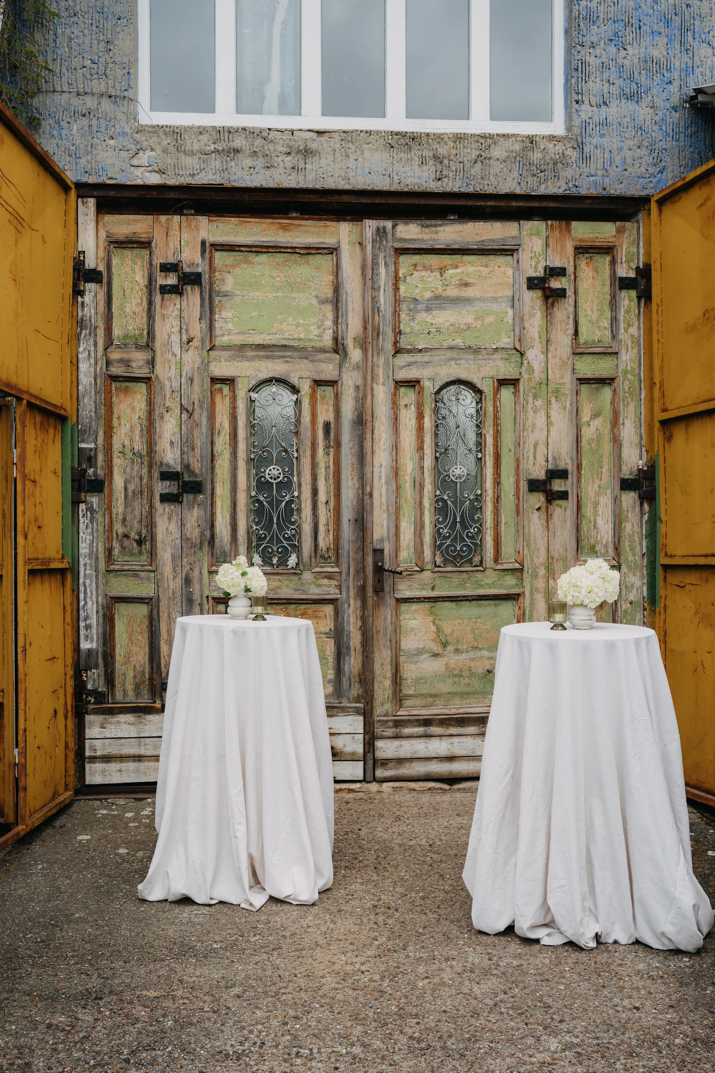 Zwei Stehtische mit Blumenschmuck vor antiken Doppeltüren, stilvolle Kulisse für Empfang, Trauung oder Sektempfang im Freien