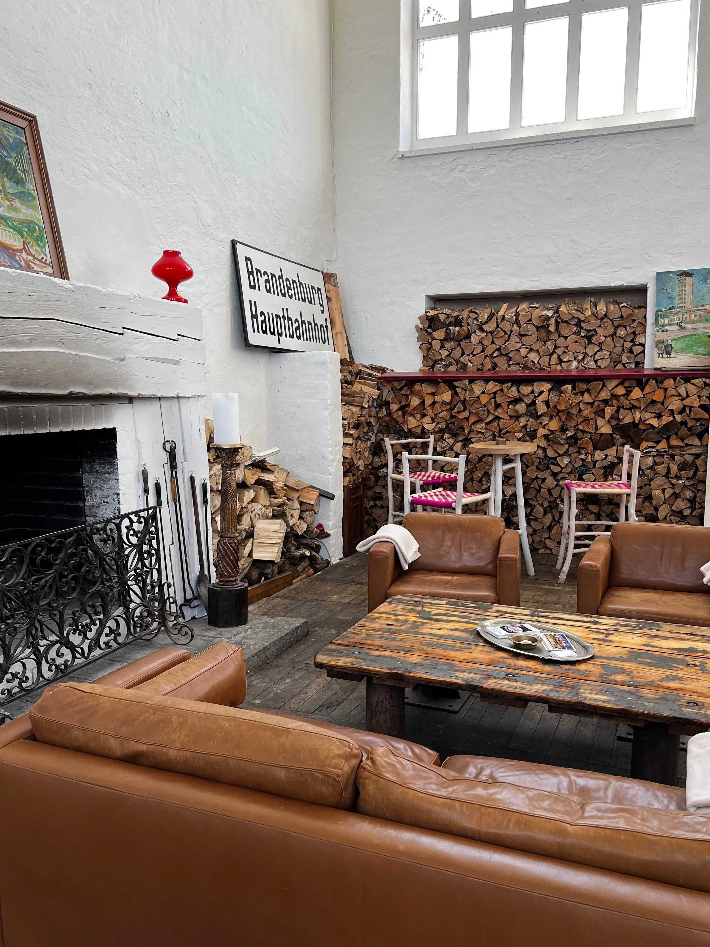 Lounge-Bereich in der Blauen Halle mit Ledersofas, Kamin, historischem Holzlager und rustikalem Couchtisch – entspannte Atmosphäre für Events bei Berlin