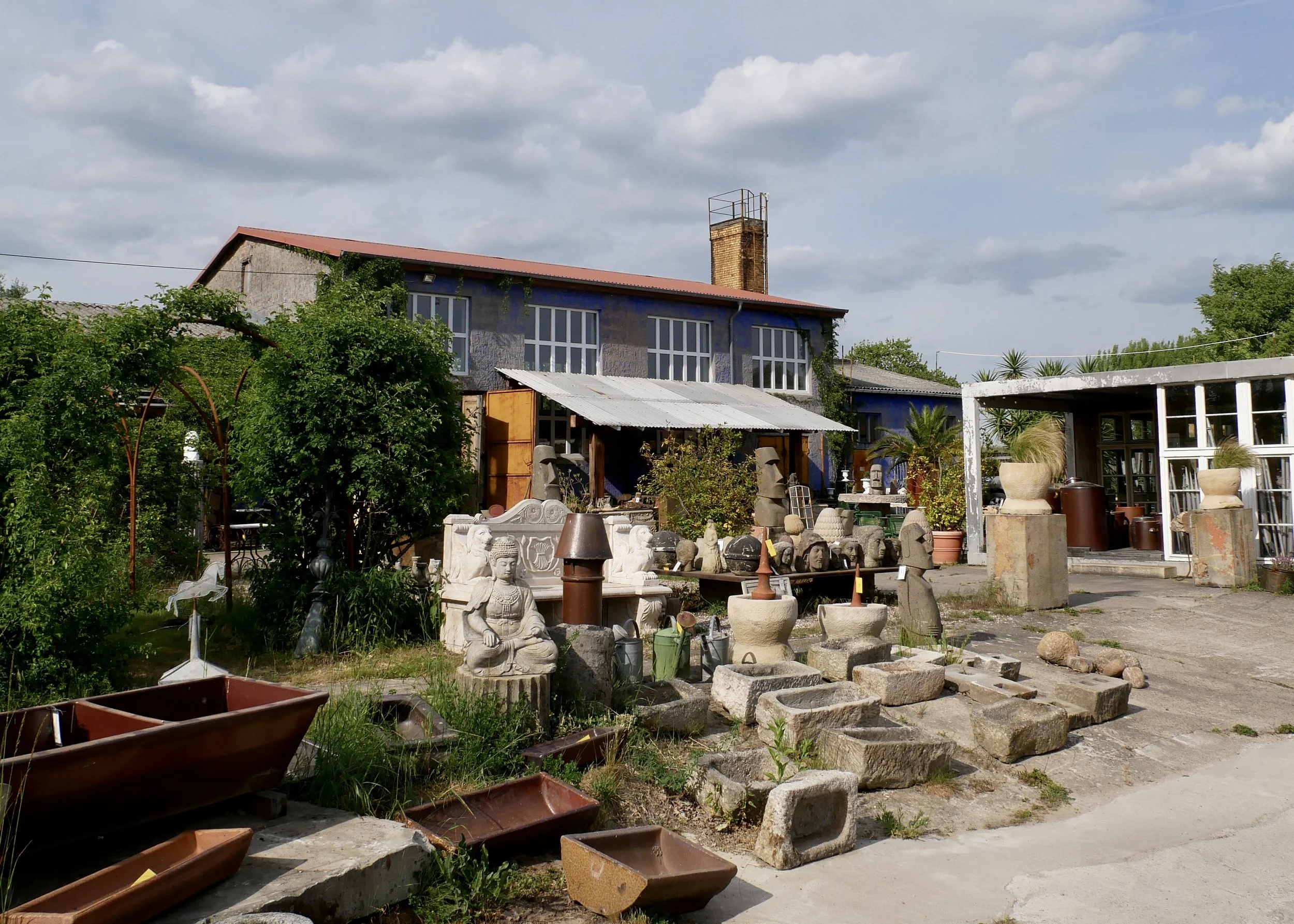Außenbereich der Blauen Halle, Naturstein-Stufen, historische Bauelemente, Pflanzeninseln und Industriefassade im kreativen Hofambiente.