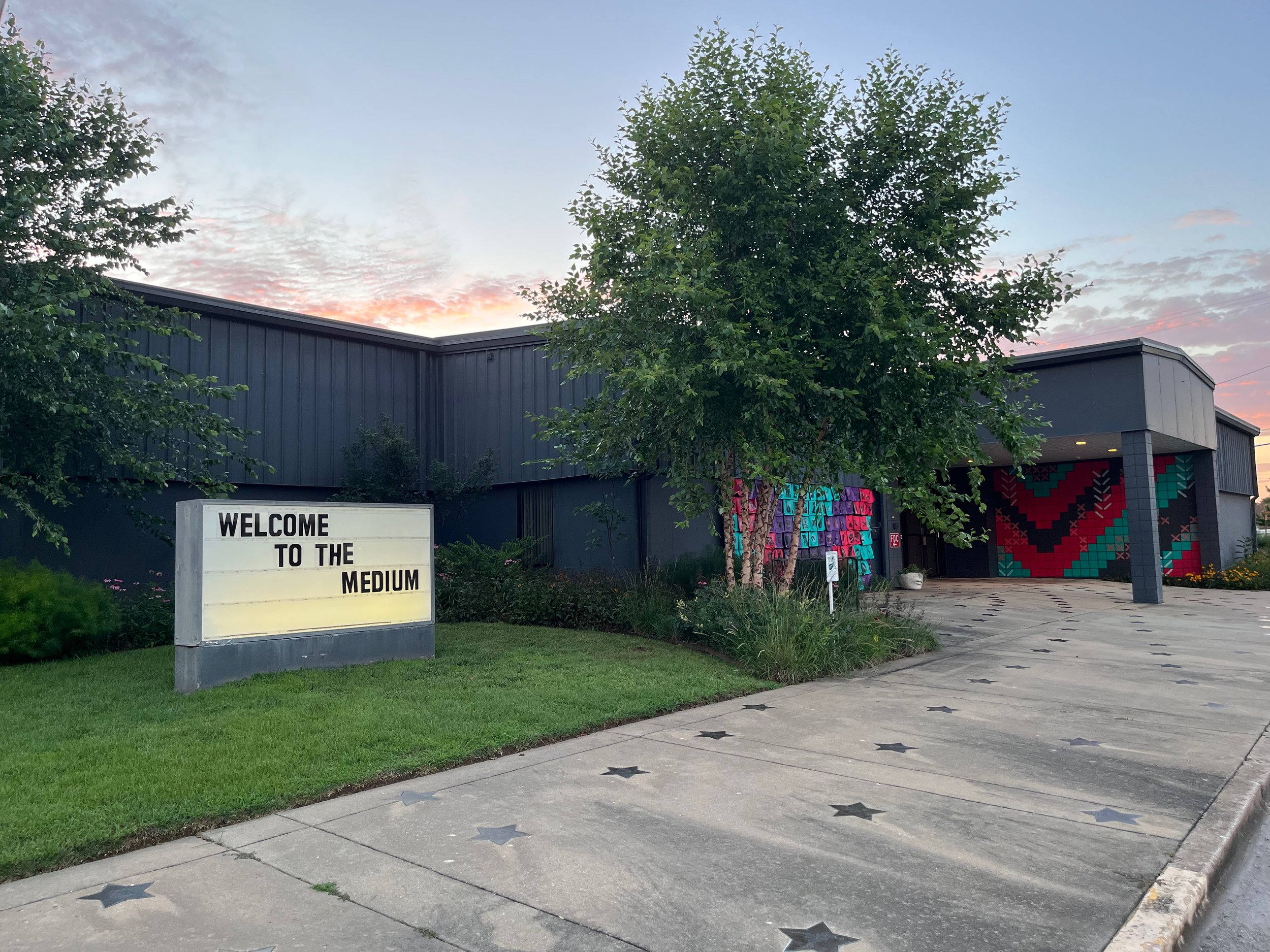 A view of a building at dusk with a marquee and installation including portraits, mural, and altar space