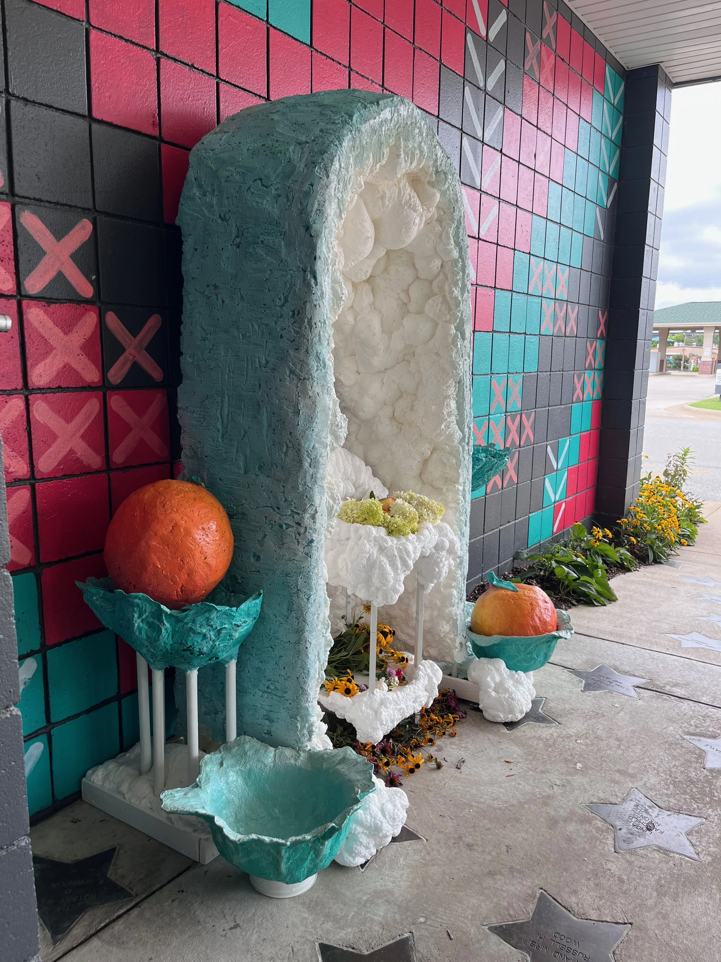 Large bowls of lettuce surround an ethereal arch and hold giant oranges, flowers, and trinkets